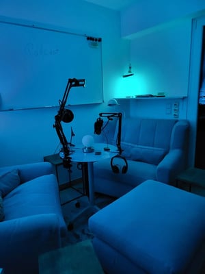 Tisch mit Podcast-Equipment, daneben zwei Sofas und ein Hocker_11zon