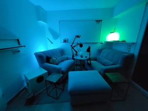 Zwei Sofas und ein Hocker, dazwischen Podcast-Equipment, grünliche Beleuchtung